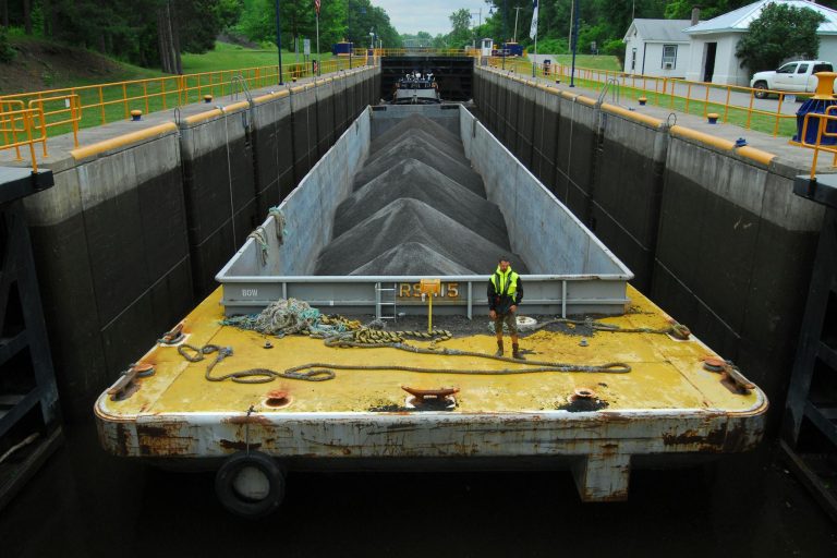 Cargo barge loaded with material in a river lock system with industrial surroundings.